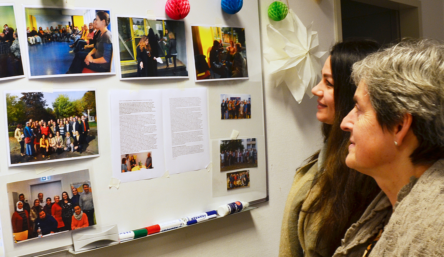 Zwei Frauen blicken auf eine Magnetwand voller Fotos