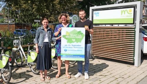 Bianca Huth, Fiona Härtel und Thorsten Werbeck halten ein Werbeplakat für den Markt der Nachhaltigkeit empor.